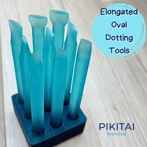 Può includere: Un set di otto strumenti per punteggiatura ovali allungati, di colore azzurro traslucido, disposti in una base rettangolare blu scuro. Ogni strumento presenta una punta piatta e angolata con marcature numeriche. Il testo Elongated Oval Dotting Tools e PIKITAI Mandala è visibile.