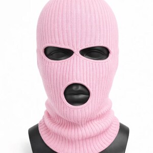 Puede incluir: Un pasamonta&ntilde;as de punto rosa claro con tres agujeros para los ojos y una abertura para la boca. El pasamonta&ntilde;as se muestra sobre una cabeza de maniqu&iacute; negra sobre un fondo blanco. La textura de punto acanalado es visible.