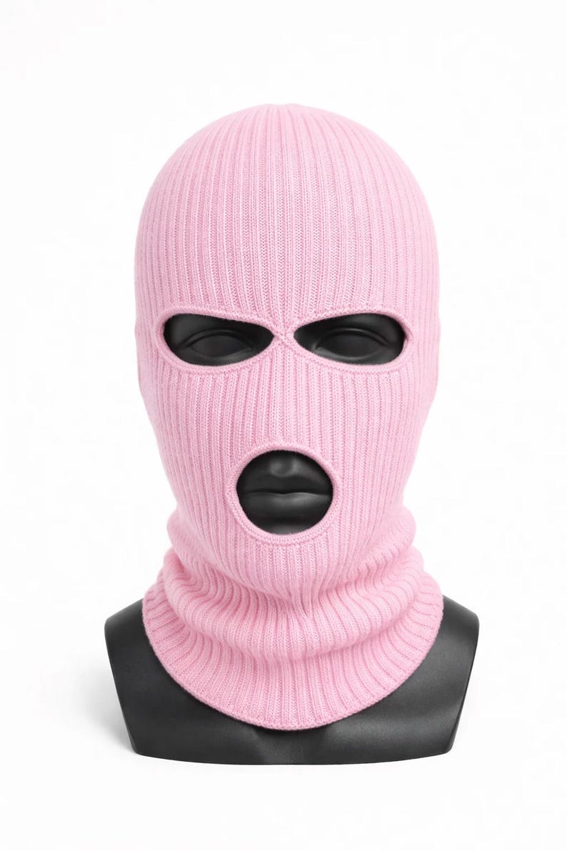 Puede incluir: Un pasamonta&ntilde;as de punto rosa claro con tres agujeros para los ojos y una abertura para la boca. El pasamonta&ntilde;as se muestra sobre una cabeza de maniqu&iacute; negra sobre un fondo blanco. La textura de punto acanalado es visible.