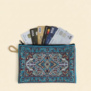 May include: A rectangular turquoise wallet with a traditional rug design, holding several credit cards. The wallet has a black zip and a beige rope loop. The credit cards are various colours and feature the Visa logo.