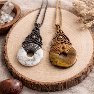 May include: Two handmade macrame stone necklaces. One features a white stone with gray veining, the other a brown and yellow stone. Both are circular with a hole in the center, suspended from a macrame cord. The text "Handmade Macrame Stone Necklaces" is at the top.
