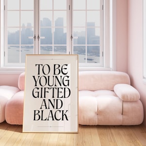May include: A framed print with the text "To be young gifted and black" in black lettering on a white background. The print is hanging on a pink wall above a pink sofa.