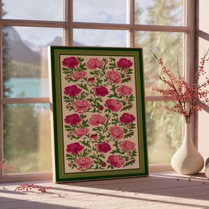 Puede incluir: Una impresi&oacute;n floral enmarcada con peon&iacute;as rosas y magenta sobre un fondo crema, enmarcada con un borde verde. La obra de arte se exhibe cerca de una ventana con vista a un lago y monta&ntilde;as. Un jarr&oacute;n con ramas rojas est&aacute; cerca.