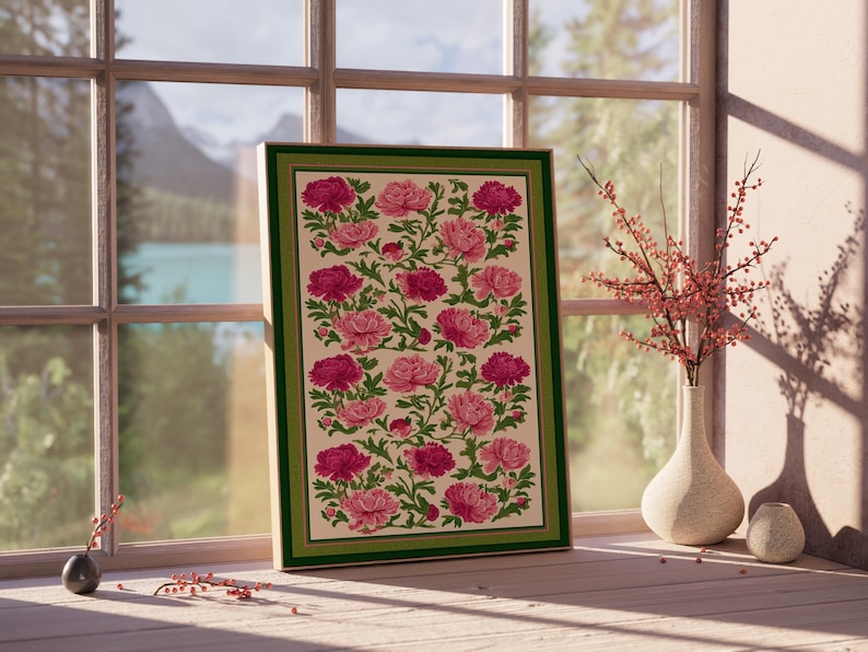 Puede incluir: Una impresi&oacute;n floral enmarcada con peon&iacute;as rosas y magenta sobre un fondo crema, enmarcada con un borde verde. La obra de arte se exhibe cerca de una ventana con vista a un lago y monta&ntilde;as. Un jarr&oacute;n con ramas rojas est&aacute; cerca.