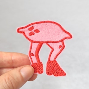May include: A pink and red embroidered patch of a cartoon animal with four legs and a long neck. The animal has a round body and a small head with three black dots.