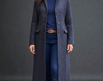 May include: A long, dark gray herringbone coat with a notched collar and three buttons. The coat has two front pockets and is worn over a navy blue turtleneck and blue jeans. A brown belt cinches the waist.