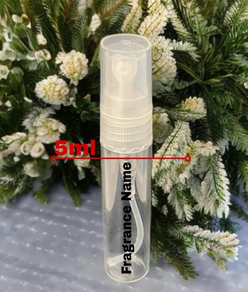 May include: A clear 5ml fragrance sample bottle with a white sprayer cap. The bottle has the words "Fragrance Name" printed vertically. The image shows the bottle against a backdrop of green and white foliage.