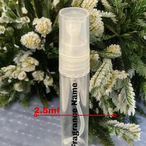 May include: A clear, cylindrical perfume sample bottle with a white spray nozzle. The bottle has the text "Fragrance Name" and "2.5ml" printed on it. The background features white and green foliage.