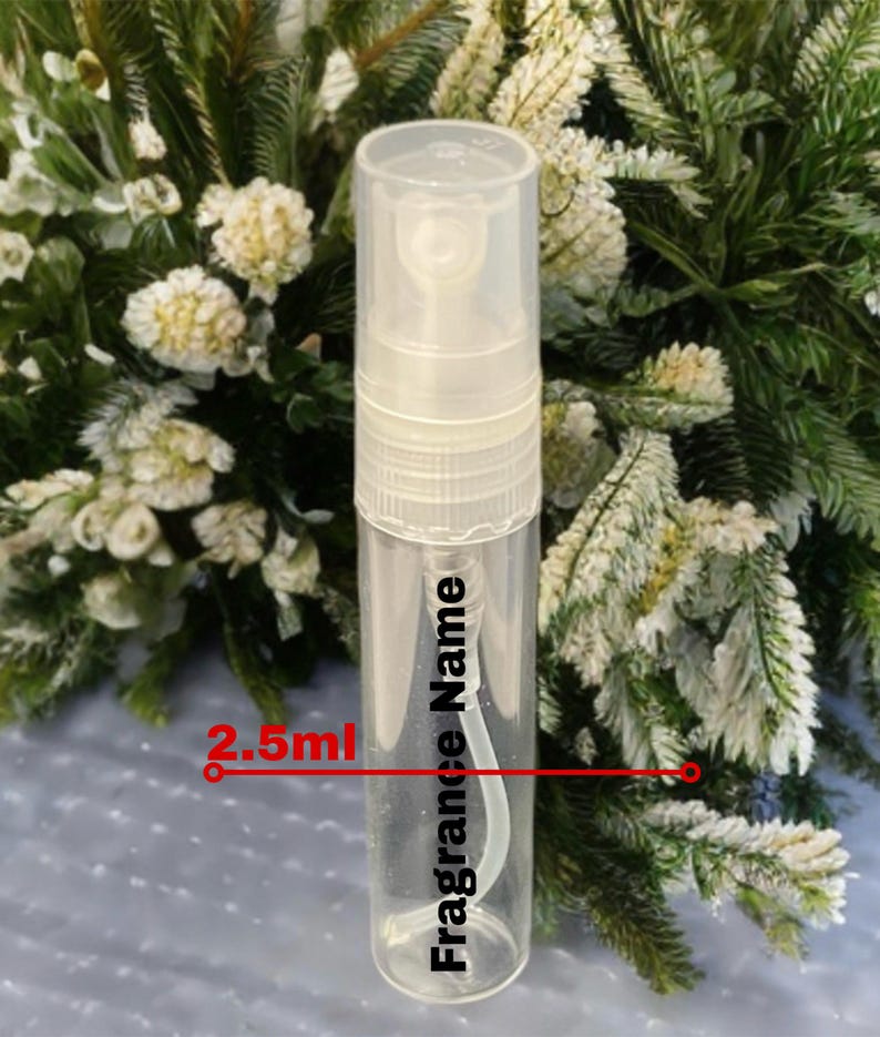 May include: A clear, cylindrical perfume sample bottle with a white spray nozzle. The bottle has the text "Fragrance Name" and "2.5ml" printed on it. The background features white and green foliage.