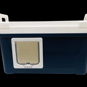 May include: A navy blue and white pet carrier with a cat door. The carrier has a rectangular shape with a white top and handles. The cat door is a square shape with a clear flap. The carrier is designed for pet travel.