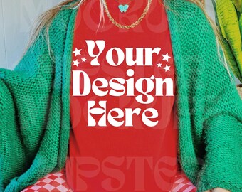 May include: A red t-shirt with the text "Your Design Here" in white, worn with a green cardigan and pink and red checkered trousers. The person is wearing a gold necklace with a turquoise butterfly pendant and black trainers.