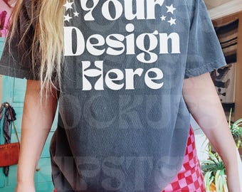 May include: A grey t-shirt with the text "Your Design Here" in white, with star accents. The person is wearing a gold chain and red and pink checkered trousers. The shirt is a relaxed fit.