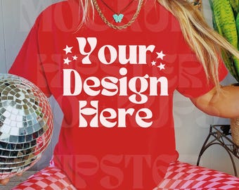 May include: A red t-shirt with the text "Your Design Here" in white, worn with red and pink checkered trousers. The person is wearing a gold chain necklace with a turquoise butterfly pendant and black trainers.