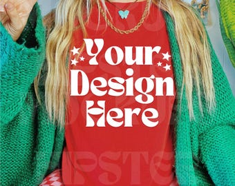May include: A red t-shirt with the text "Your Design Here" in white, paired with a green cardigan and pink checkered trousers. A gold chain necklace with a turquoise butterfly pendant is visible. Black and white trainers complete the outfit.