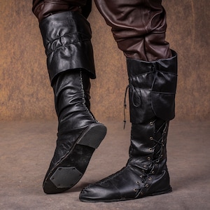 Op de afbeelding: Een paar zwarte leren laarzen met veters en een omslagmanchet. De laarzen zijn gedragen en hebben een verweerde look.