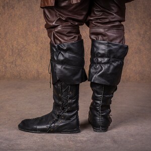 Op de afbeelding: Een paar zwarte leren laarzen met veters aan de voorkant en een omslag aan de bovenkant.