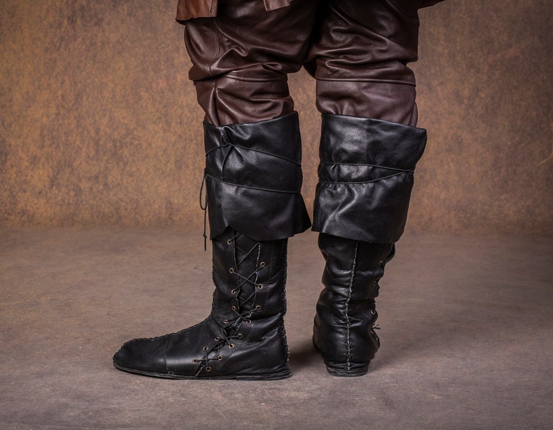 Op de afbeelding: Een paar zwarte leren laarzen met veters aan de voorkant en een omslag aan de bovenkant.