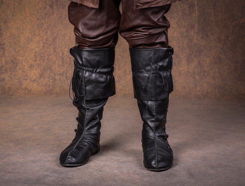 Op de afbeelding: Een paar zwarte leren laarzen met veters en gespen. De laarzen hebben een puntige neus en een lage hak.