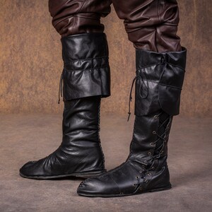 Op de afbeelding: Een paar zwarte leren laarzen met veters aan de voorkant en een omslagmanchet aan de bovenkant.