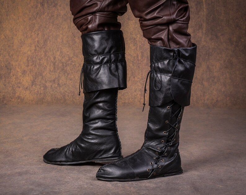 Op de afbeelding: Een paar zwarte leren laarzen met veters aan de voorkant en een omslagmanchet aan de bovenkant.