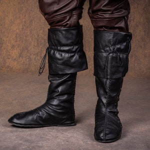 Op de afbeelding: Een paar zwarte leren laarzen met veters en een omslagmanchet. De laarzen zijn gedragen en hebben een verweerde look.