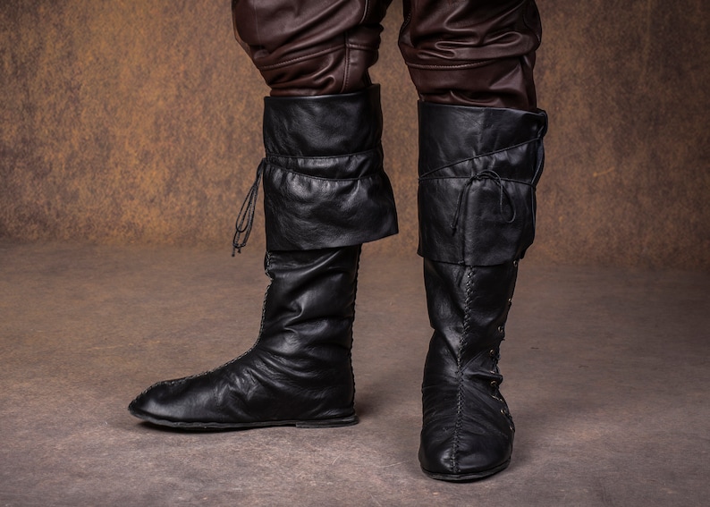 Op de afbeelding: Een paar zwarte leren laarzen met veters en een omslagmanchet. De laarzen zijn gedragen en hebben een verweerde look.