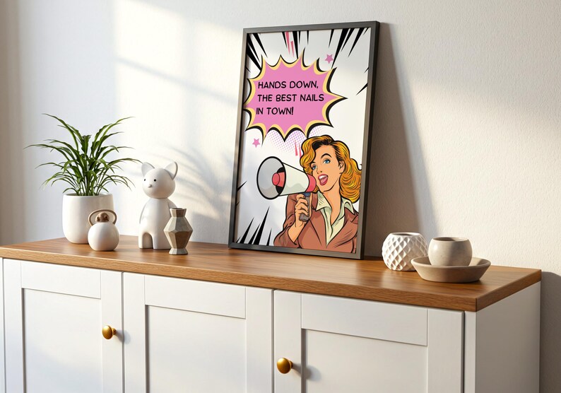 Modern shelf styling with a black framed pop art beauty poster. "Best Nails In Town" sign displayed on a white cabinet. Bold graphic design with Ben-Day dots and comic book elements. Unique gift idea for salon grand openings.