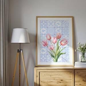 Digital wall art featuring a watercolor pink tulip bouquet on a blue and white Delftware tile background. This botanical poster is ideal for cottagecore, farmhouse, and Mediterranean-style kitchen or bathroom decor. With a background resembling Portuguese azulejo tiles and vibrant spring flowers, it offers a fresh and airy look. This printable image is perfect as a Mother's Day gift or seasonal spring decor.