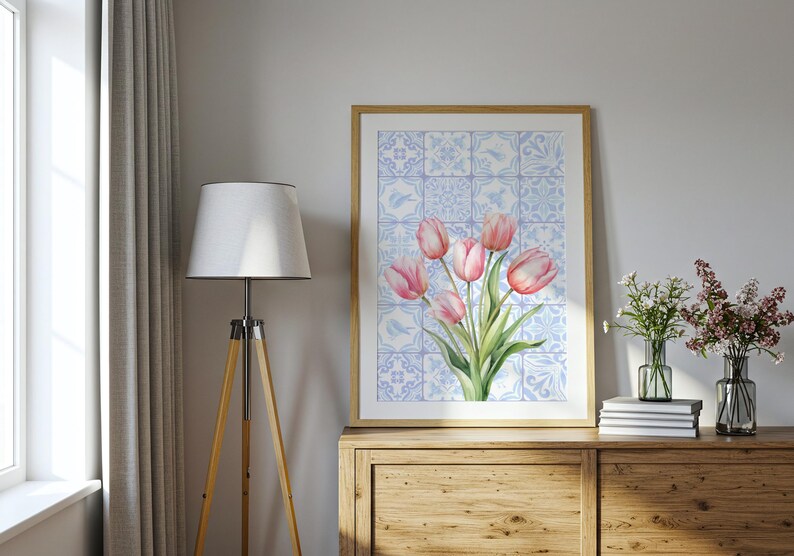 Digital wall art featuring a watercolor pink tulip bouquet on a blue and white Delftware tile background. This botanical poster is ideal for cottagecore, farmhouse, and Mediterranean-style kitchen or bathroom decor. With a background resembling Portuguese azulejo tiles and vibrant spring flowers, it offers a fresh and airy look. This printable image is perfect as a Mother's Day gift or seasonal spring decor.