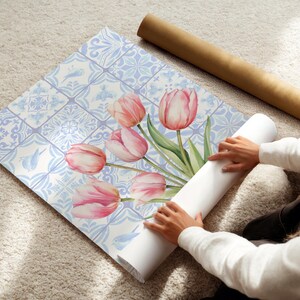 Digital wall art featuring a watercolor pink tulip bouquet on a blue and white Delftware tile background. This botanical poster is ideal for cottagecore, farmhouse, and Mediterranean-style kitchen or bathroom decor. With a background resembling Portuguese azulejo tiles and vibrant spring flowers, it offers a fresh and airy look. This printable image is perfect as a Mother's Day gift or seasonal spring decor.
