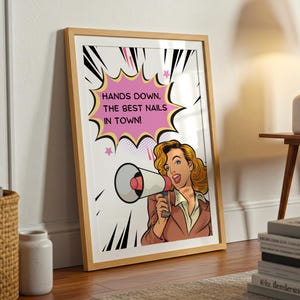 Large framed nail salon sign leaning against a wall on wooden flooring. Vintage pop art design with a funny "Best Nails in Town" quote. Eye-catching decor for a manicurist's studio or pedicure station to attract clients.