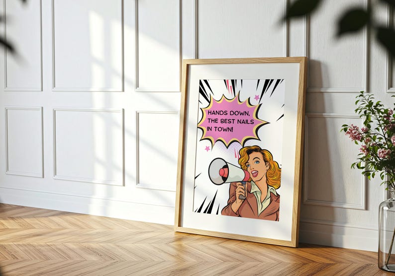 Close up view of a framed manicurist gift poster in a sunlit room. Detailed retro illustration of a woman shouting into a megaphone. High-quality printable wall art with a "Hands Down" nail pun message.