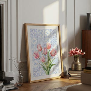 Digital wall art featuring a watercolor pink tulip bouquet on a blue and white Delftware tile background. This botanical poster is ideal for cottagecore, farmhouse, and Mediterranean-style kitchen or bathroom decor. With a background resembling Portuguese azulejo tiles and vibrant spring flowers, it offers a fresh and airy look. This printable image is perfect as a Mother's Day gift or seasonal spring decor.