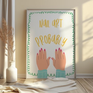 May include: A framed print with the words "NAIL ART PROBABLY" in yellow script. The print features cartoon hands with pink nails and blue sleeves, set against a white background with a green border. The artwork is displayed on a wooden floor.