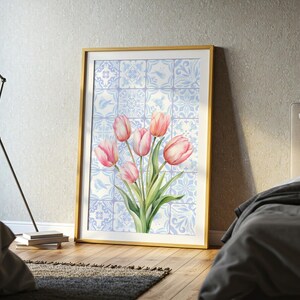 Digital wall art featuring a watercolor pink tulip bouquet on a blue and white Delftware tile background. This botanical poster is ideal for cottagecore, farmhouse, and Mediterranean-style kitchen or bathroom decor. With a background resembling Portuguese azulejo tiles and vibrant spring flowers, it offers a fresh and airy look. This printable image is perfect as a Mother's Day gift or seasonal spring decor.