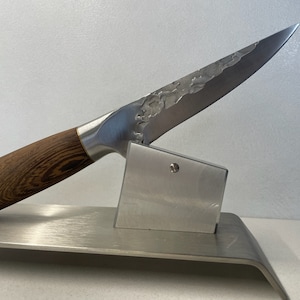May include: A silver knife with a wooden handle and a textured blade is displayed on a silver stand.