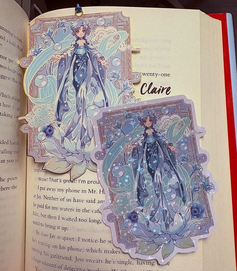 May include: Two decorative bookmarks featuring a detailed illustration of a woman in a flowing blue gown, surrounded by bubbles and floral accents. The bookmarks are set against the pages of a book. The word "Claire" is visible on the page.