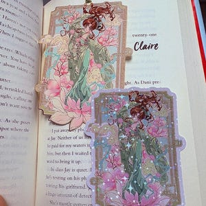 May include: Two decorative bookmarks featuring an anime-style illustration of a woman in a flowing green gown, surrounded by pink lotus flowers and clouds. The bookmarks are on a book, with the word "Claire" visible.