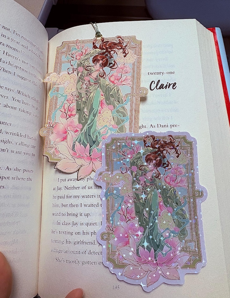 May include: Two decorative bookmarks featuring an anime-style illustration of a woman in a flowing green gown, surrounded by pink lotus flowers and clouds. The bookmarks are on a book, with the word "Claire" visible.