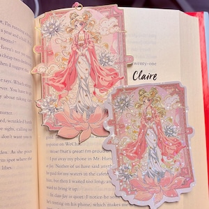 May include: Two decorative bookmarks and a sticker featuring a pink-robed anime character with blonde hair, set against a floral and cloud background. The text "twenty-one Claire" is visible on the book page. The design includes lotus flowers and a decorative border.