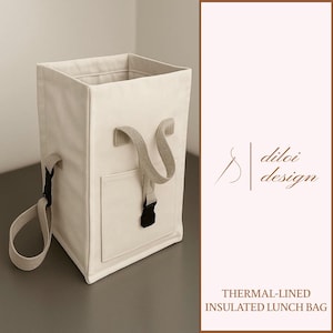 May include: Cream-coloured thermal-lined insulated lunch bag with a rectangular shape. Features a small front pocket, a handle, and a shoulder strap. The bag has a black buckle closure and the text "diloi design".