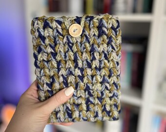 May include: A crocheted phone case with a blue, green, and beige color pattern. The case has a wooden button closure.