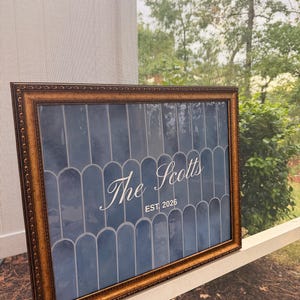 May include: A rectangular wall sign in an ornate bronze-colored frame featuring a dark blue background with a repeating vertical arch pattern. The text "The Scotts" is printed in white script, with "EST. 2026" centered underneath in white.