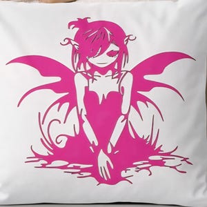 May include: White square pillow featuring a magenta illustration of a fairy-like figure with wings. The design is a silhouette of a seated person with long hair and a dress. The pillow is on a white surface.