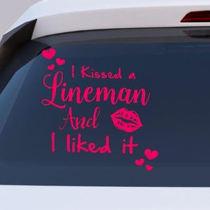 May include: A pink decal on a car window with the text "I Kissed a Lineman And I liked it" and a kiss mark graphic. Small pink hearts are also included in the design.