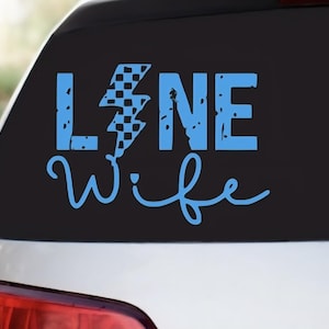 May include: A blue vinyl decal with the words "LANE Wife" in a distressed font. The letter "L" is stylized with a lightning bolt design, incorporating a checkered flag pattern. The decal is applied to a car window.
