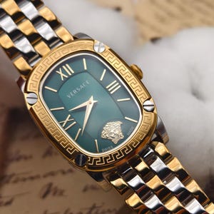 Puede incluir: Un reloj Versace dorado y plateado con esfera verde. El reloj tiene una esfera rectangular con n&uacute;meros romanos y agujas doradas. La correa del reloj es una combinaci&oacute;n de eslabones dorados y plateados. El logotipo de Versace y una cabeza de Medusa son visibles en la esfera.