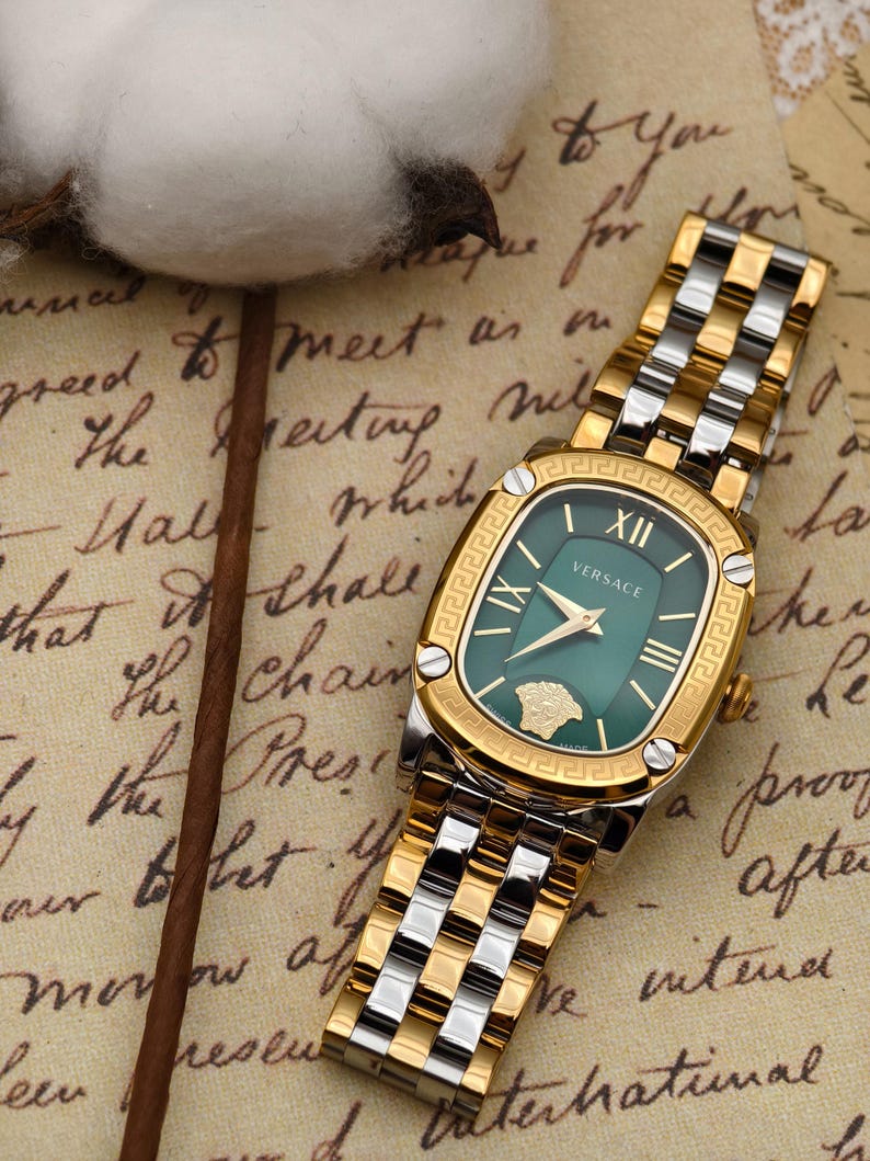 Puede incluir: Un reloj Versace dorado y plateado con esfera verde. El reloj tiene una esfera rectangular con n&uacute;meros romanos y un bisel dorado. La correa es una combinaci&oacute;n de eslabones dorados y plateados.
