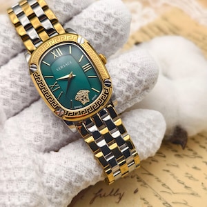 Puede incluir: Reloj Versace bicolor en oro y plata con esfera verde. El reloj tiene una esfera rectangular con n&uacute;meros romanos y un bisel dorado. La correa es una combinaci&oacute;n de eslabones dorados y plateados. El logotipo de Versace es visible.