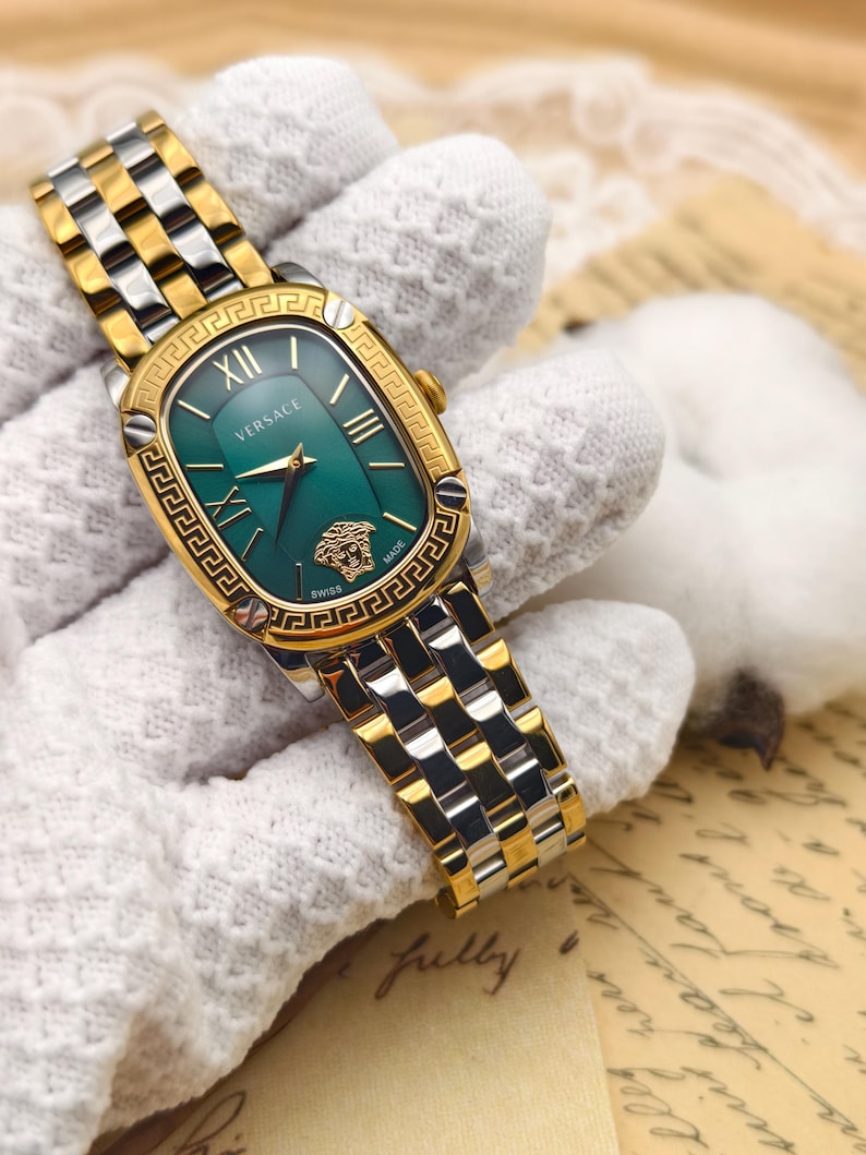 Puede incluir: Reloj Versace bicolor en oro y plata con esfera verde. El reloj tiene una esfera rectangular con n&uacute;meros romanos y un bisel dorado. La correa es una combinaci&oacute;n de eslabones dorados y plateados. El logotipo de Versace es visible.
